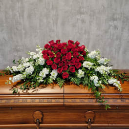 Red roses and white flowers arranged on a wooden casket