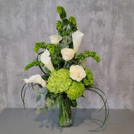 Green hydrangeas and white calla lilies in a glass vase