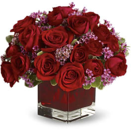 Red roses and small purple flowers arranged in a square glass vase