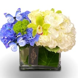 Blue and white floral arrangement in a square glass vase with butterfly accents