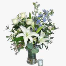 White lilies and roses in a glass vase with a small candle beside it