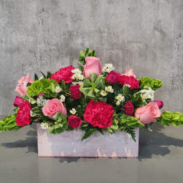 Pink and red flower arrangement in a pale wooden box