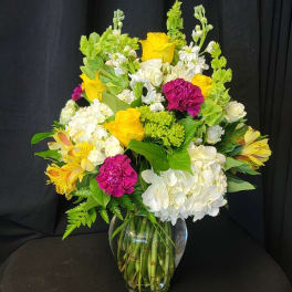 Mixed bouquet of yellow, white, and magenta flowers in a clear glass vase
