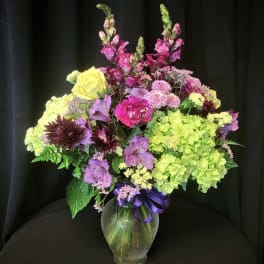 Mixed bouquet of purple, pink, and yellow flowers in a glass vase