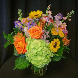 Colorful mixed bouquet with hydrangea, roses, and sunflowers in a glass vase