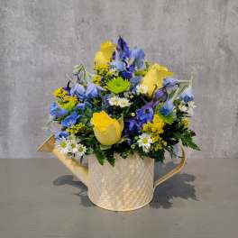 Blue and yellow mixed bouquet in a cream watering-can container