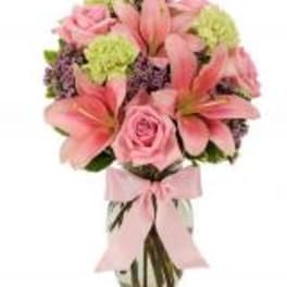 Pink lilies and roses arranged in a vase with a pink ribbon