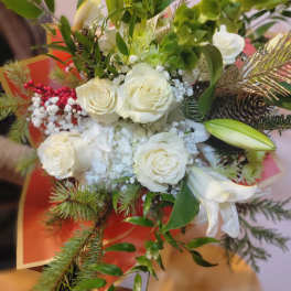White roses and lilies arranged with greenery and pinecones
