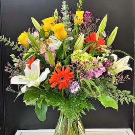 Mixed bouquet of lilies, gerbera daisies, and roses in a glass vase