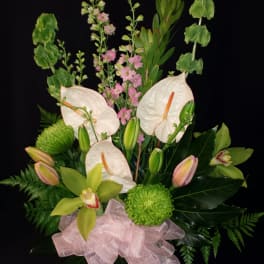 White anthuriums and pink orchids in a glass vase with a pink bow