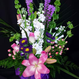 Pink lilies and purple flowers in a glass vase with a purple ribbon