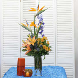 Tall tropical flower arrangement in a clear glass vase with orange and blue blooms