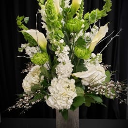 Tall white floral arrangement with calla lilies and green blooms in a square vase