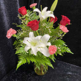 Bouquet of red roses, white lilies, and pink carnations in a glass vase