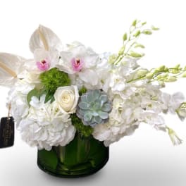 White floral arrangement in a green glass vase with orchids and hydrangeas