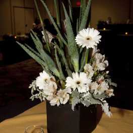 White gerbera daisies and pale flowers in a black vase with tall spiky foliage
