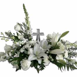Low white floral spray with lilies, roses, and a central silver cross accent