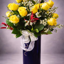 Yellow roses arranged in a tall blue vase with a white ribbon bow