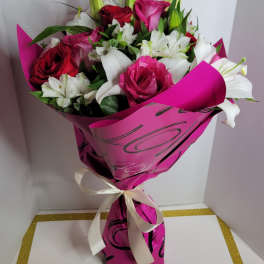 Bouquet of pink and red roses with white lilies wrapped in bright pink paper