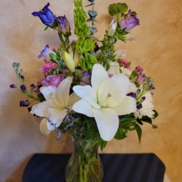 Mixed bouquet of white lilies, purple blooms, and pink roses in a glass vase