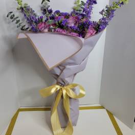 Purple and pink bouquet wrapped in lavender paper with a yellow ribbon