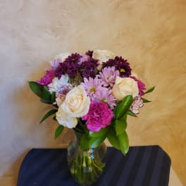 Mixed bouquet of white roses, pink daisies, and purple carnations in a glass vase