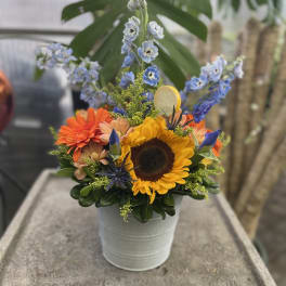 Bright mixed bouquet in a white metal bucket with a sunflower and blue flowers