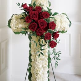 Cross-shaped floral tribute with red roses and white flowers on a stand