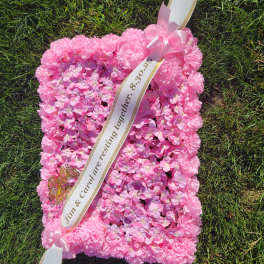 Pink floral sympathy pillow with ribbon sash on grass