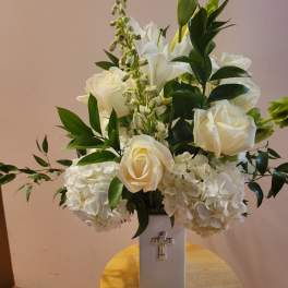 White roses and hydrangeas in a tall vase with a cross emblem
