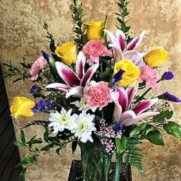 Mixed bouquet with pink lilies, yellow roses, and white daisies in a glass vase