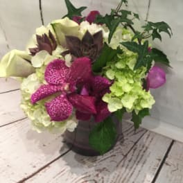 Low arrangement of white and green hydrangeas with bright pink orchids and calla lilies in a glass vase with trailing ivy