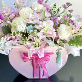 Pink and white floral arrangement in a heart-shaped box with a ribbon bow