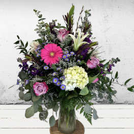 Tall mixed bouquet of pink gerbera, roses, white lilies and green hydrangea in a clear glass vase