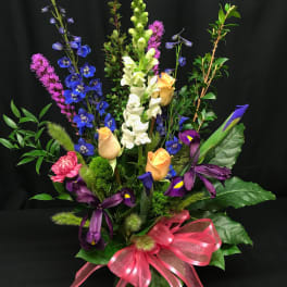 Tall mixed bouquet with blue, white, purple, and peach flowers in a glass vase