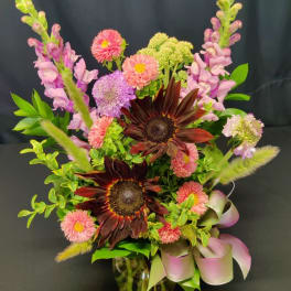 Mixed bouquet with dark sunflowers, pink blooms, and a glass vase