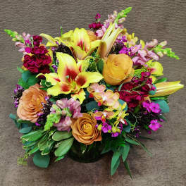 Mixed bouquet with yellow lilies, peach roses, and pink flowers in a low vase