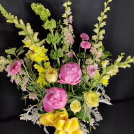 Pink peonies and yellow flowers in a vase with a yellow ribbon