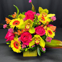 Bright bouquet of pink roses, yellow orchids, and gerbera daisies in a square vase