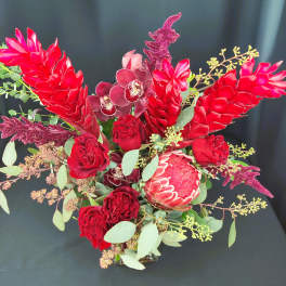 Red tropical bouquet with orchids, roses, and protea in a vase