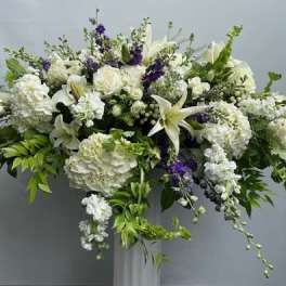Large white floral arrangement with lilies and roses on a pedestal