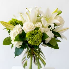 White lilies and roses in a clear glass vase with green accents
