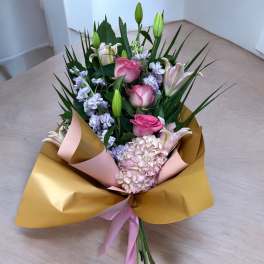 Bouquet of pink roses, lilies, and pale hydrangea wrapped in gold paper