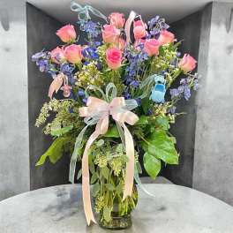Pink roses and blue flowers in a glass vase with pastel ribbons