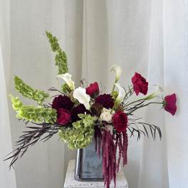 Tall floral arrangement with white calla lilies, magenta roses, and green hanging blooms in a vase.
