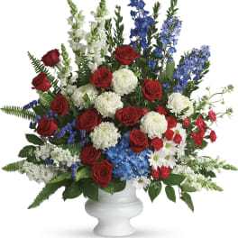 Red roses, white mums, and blue delphinium in a white vase