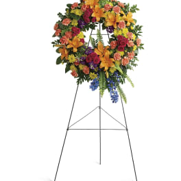 Standing floral wreath on an easel with orange lilies, roses, and mixed blooms