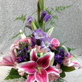 Pink lilies and purple flowers in a tall glass vase
