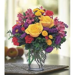 Bouquet of yellow roses, pink alstroemeria, and purple flowers in a clear vase