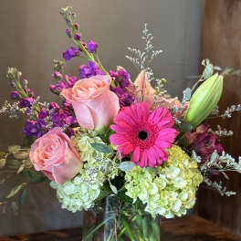Mixed bouquet of pink roses, hot pink gerbera, purple flowers and green hydrangeas in a clear glass vase